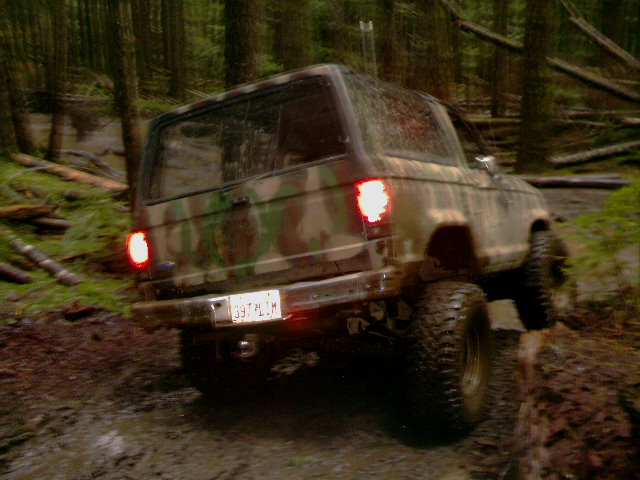 Camo two-door 4x4 SUV from behind with brake lights on, flexing on a muddy trail