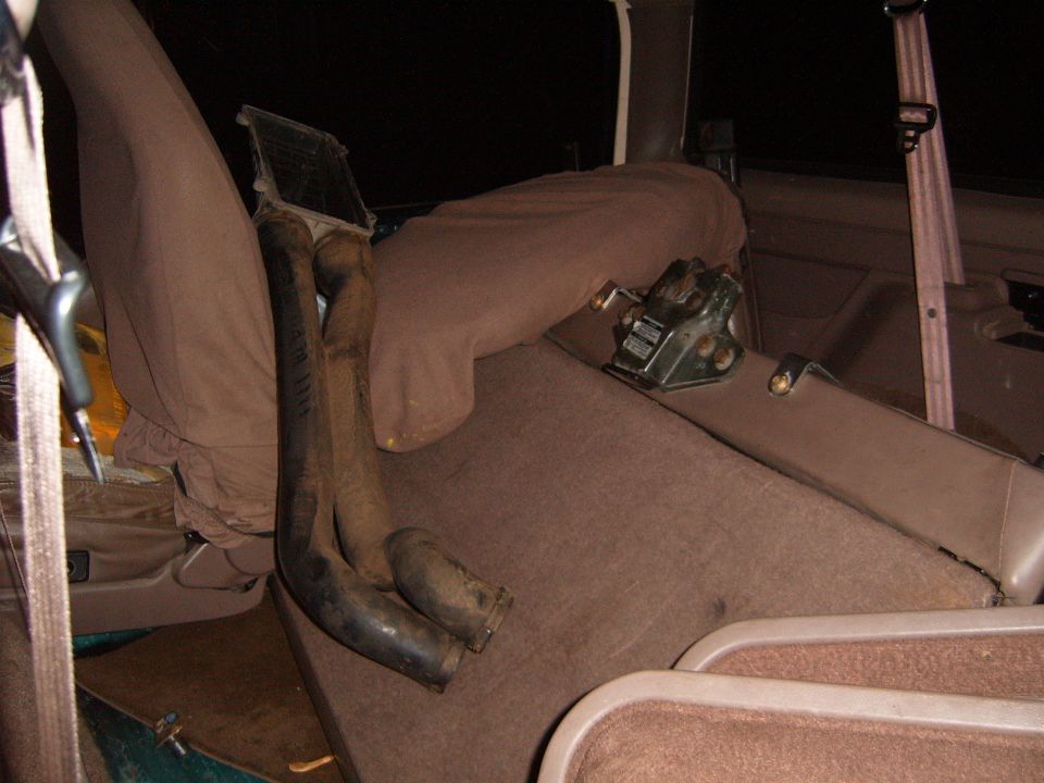 Tan SUV rear interior with used rubber hoses and metal bracket laid on the carpeted cargo area