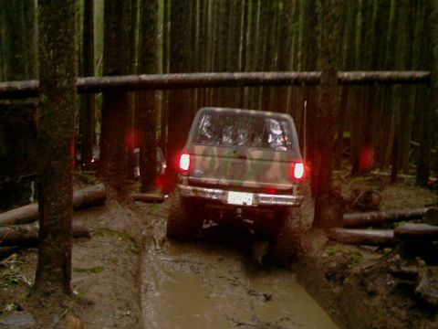 1987 Ford Bronco II - An off-road vehicle with camouflage paint navigates a challenging muddy track in a dense forest.