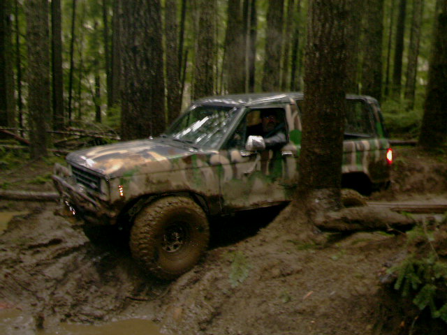 Camouflaged SUV driving through mud in a forest