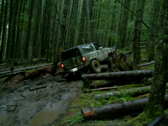 1987 Ford Bronco II navigating a muddy forest trail with fallen trees