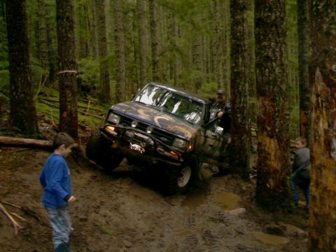 1987 Ford Bronco II - A 1987 Ford Bronco II navigates a steep, muddy trail through a dense forest.