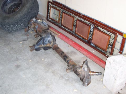 1991 Ford Bronco - A disassembled vehicle axle sits on a concrete floor next to a spare tire and decorative wall art.