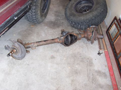 1991 Ford Bronco - A disassembled front axle assembly lies on a concrete floor near a red vehicle.