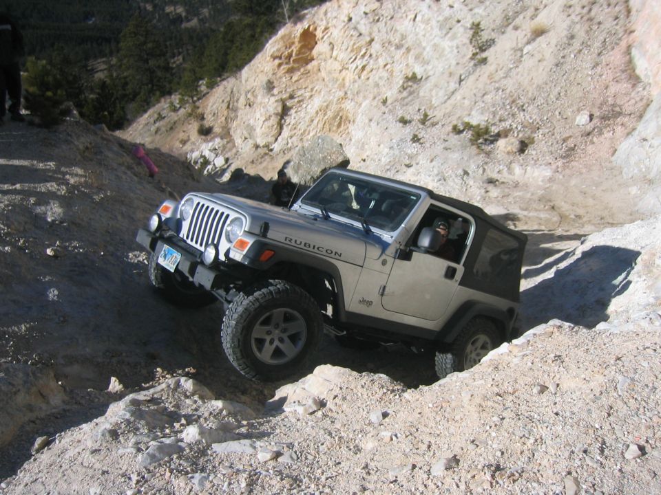 Silver Jeep Wrangler TJ Rubicon crawling down a steep rocky ledge, front three-quarter view