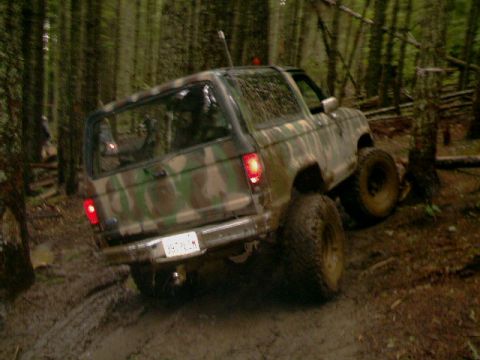 1987 Ford Bronco II - Camouflaged 1987 Ford Bronco II navigates a muddy, wooded off-road path.