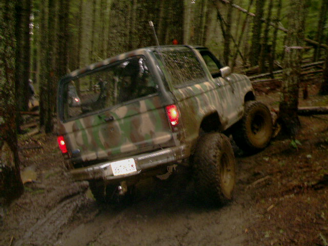 Camo lifted Bronco II with brake lights on climbing a muddy forest trail rut