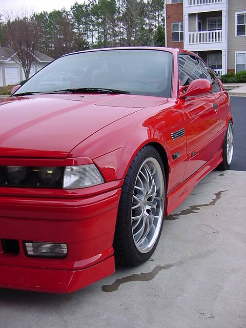 1995 BMW M3 - A red 1995 BMW M3 coupe is shown from a 3/4 front angle, parked on a concrete surface.