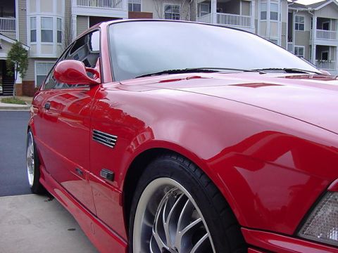 1995 BMW M3 - A red 1995 BMW M3 coupe is shown from the front quarter angle, parked in front of an apartment complex.