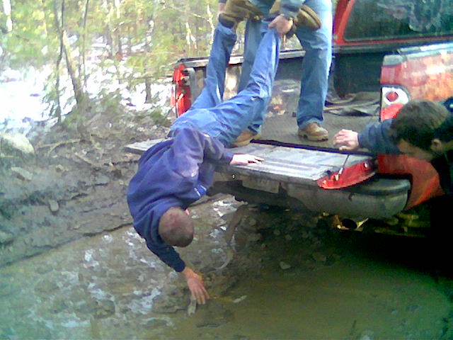 guy being pulled from mud pit by friends next to a red pickup truck