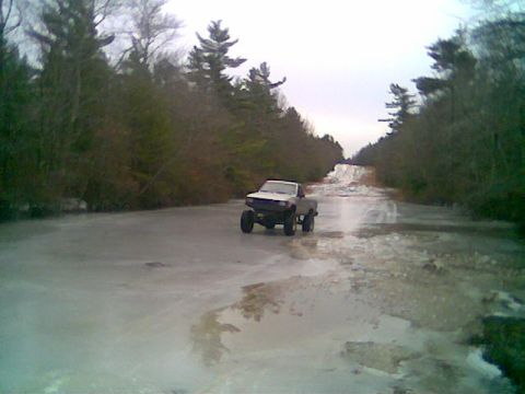 1976 GMC C/K Pickup - A pickup truck navigates a slippery, icy road surrounded by trees.