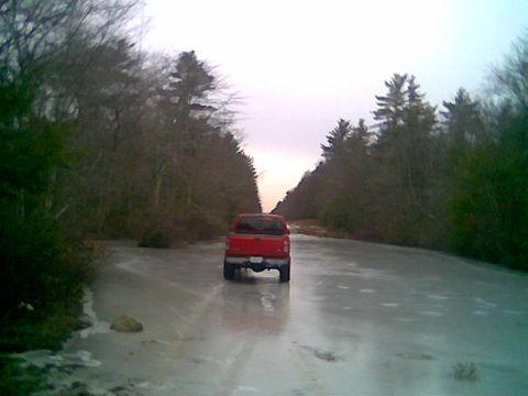 1976 GMC C/K Pickup - A red pickup truck navigates a slippery, ice-covered road through a wooded area during twilight.