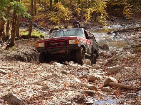 1977 Ford F-150 - Off-road SUV tackles a challenging rocky stream during autumn.