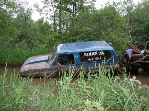 1977 Ford F-150 - A blue off-road vehicle is submerged in mud, with another vehicle partially visible behind it, flying an American flag.