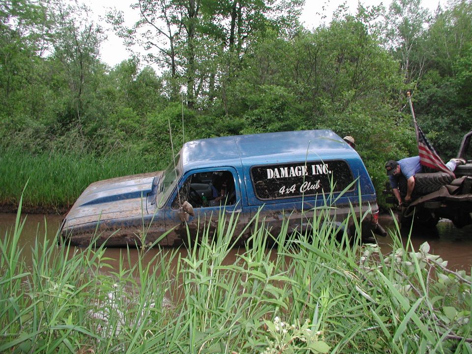 Blue off-road vehicle stuck in mud with "DAMAGE INC. 4x4 Club" on window