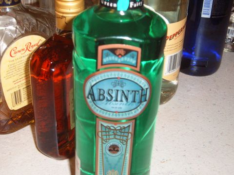 1988 Ford Bronco - A collection of alcohol bottles, including a prominent green bottle of Absinthe, are arranged on a countertop.