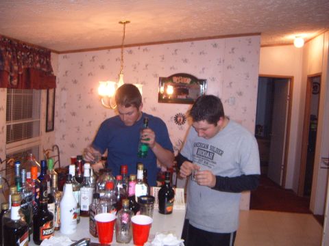 1988 Ford Bronco - Men pour drinks at a table covered with various bottles of alcohol and red cups.