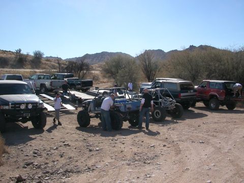 1984 Ford Bronco - A collection of modified off-road vehicles and trucks are gathered in a dry, outdoor area.