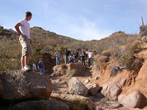 1984 Ford Bronco - A group of people stand on rocks in a desert canyon, with a cactus visible in the background.