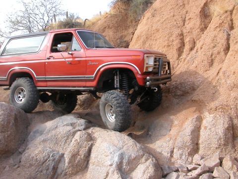 1984 Ford Bronco - This red Ford Bronco is shown off-roading on a steep, rocky incline.