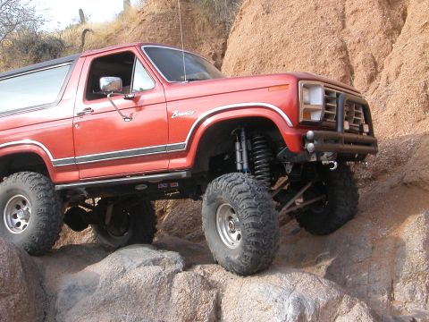 1984 Ford Bronco - This red 1984 Ford Bronco is shown off-roading on a rocky trail, demonstrating its lifted suspension and capabilities.
