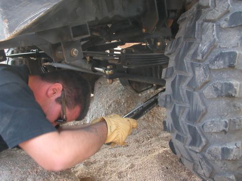 1984 Ford Bronco - A person uses a wrench to adjust the steering linkage on a vehicle's undercarriage.