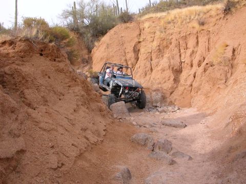 1984 Ford Bronco - Two people in an off-road buggy traverse a challenging rocky path in a desert canyon.
