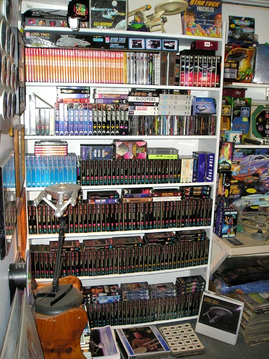 White shelves filled with Star Trek VHS tapes, books, and memorabilia in a collector's room