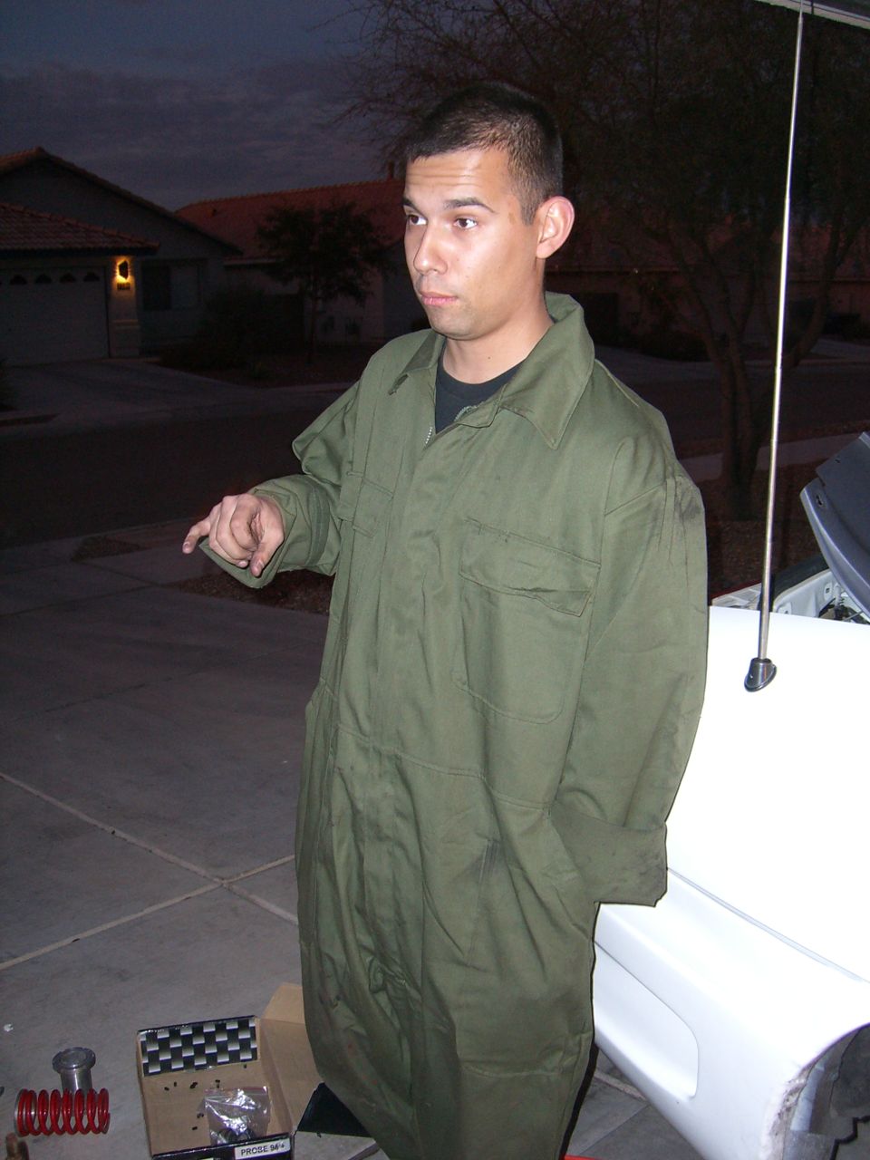 White car side view with man in green jumpsuit pointing