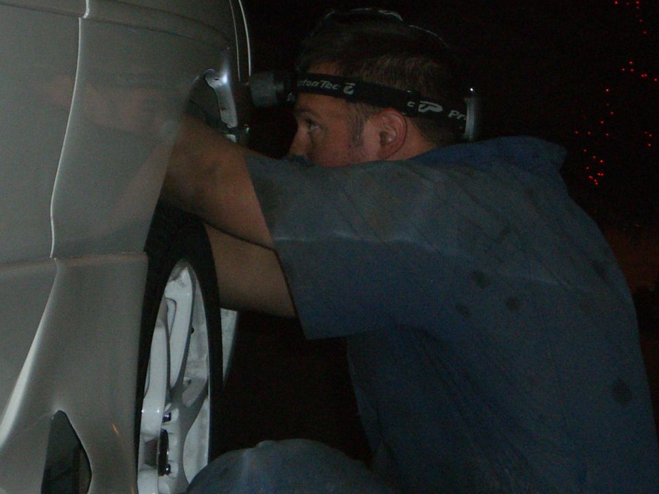 Man with headlamp working on the wheel well of a car