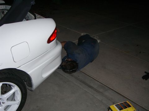 1996 Ford Probe - A person works on the rear bumper of a white 1996 Ford Probe with its trunk open.