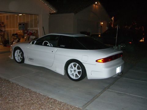 1996 Ford Probe - White 1996 Ford Probe with aftermarket wheels and body kit parked outside a garage.