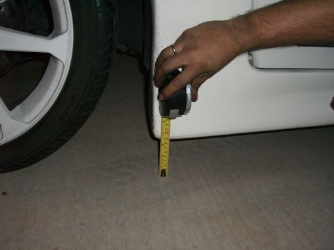 1996 Ford Probe - A hand uses a tape measure to check the ground clearance of a white vehicle's side skirt.