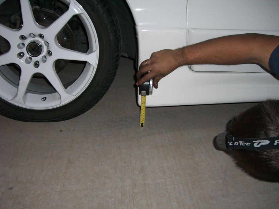 Hand holding tape measure to side skirt of white vehicle near wheel