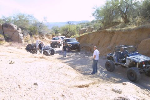 1994 Ford Bronco - A convoy of off-road vehicles, including a 1994 Ford Bronco, navigates a dry, sandy canyon.