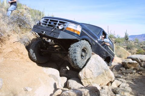 1994 Ford Bronco - Black Ford Bronco navigates a rocky desert trail with a modified front bumper.