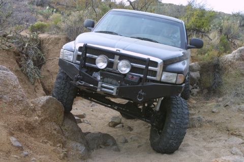 1994 Ford Bronco - This modified Dodge Ram is tackling a challenging off-road trail with its front tire high on a rock.
