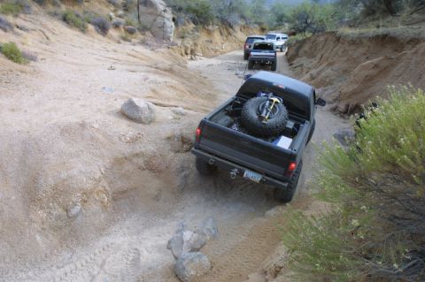 1994 Ford Bronco - A convoy of off-road vehicles navigates a challenging dirt track through a canyon.
