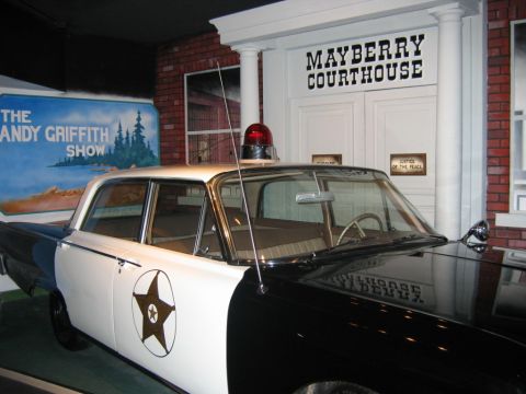 1985 Ford Crown Victoria LTD - A replica police car, likely from The Andy Griffith Show, is parked in front of a 'Mayberry Courthouse' display.