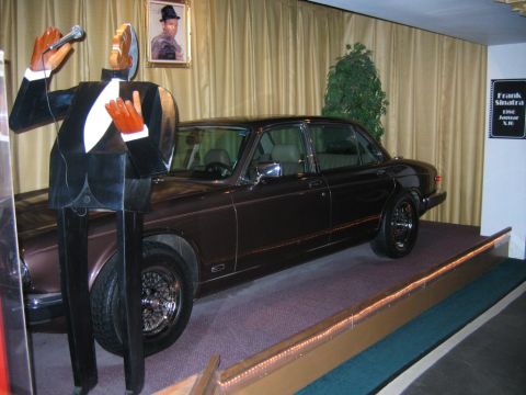 1985 Ford LTD Crown Victoria - A vintage Jaguar XJ6 is displayed next to a cutout of a singer, with a portrait of Frank Sinatra on the wall.