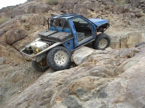 1989 Ford Bronco - A heavily modified blue off-road vehicle tackles a challenging rocky trail.