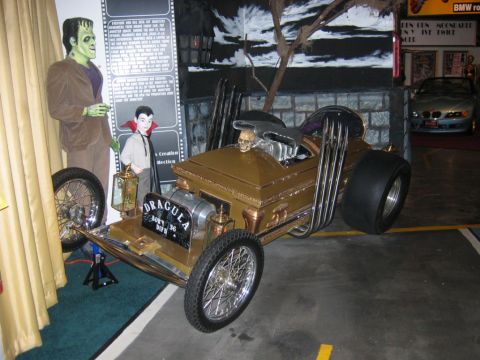 1985 Ford LTD Crown Victoria - A custom coffin hot rod is displayed next to monster figures, with a blue convertible visible in the background.