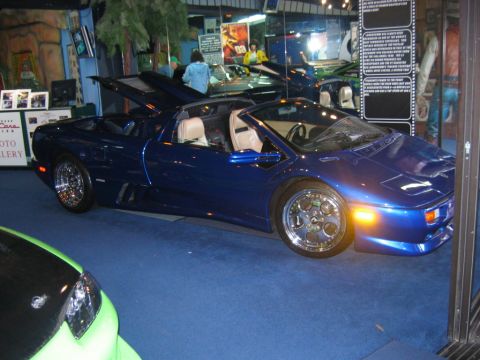 1985 Ford LTD Crown Victoria - A blue convertible sports car is displayed indoors with its hood open, next to a green vehicle.