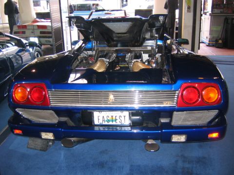 1985 Ford LTD Crown Victoria - Rear view of a blue sports car with its engine compartment open, displaying gold-colored engine components.