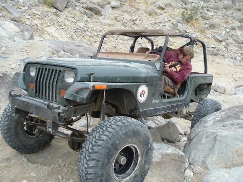1989 Ford Bronco - A green Jeep Wrangler navigates a rocky trail with a person inside.