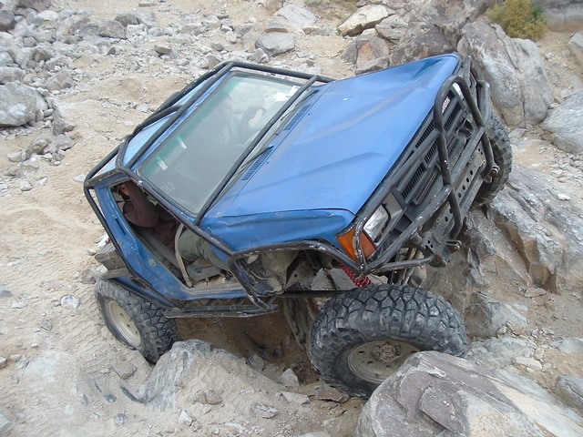 Blue caged 4x4 rock crawler flexing over boulders on a rocky desert trail