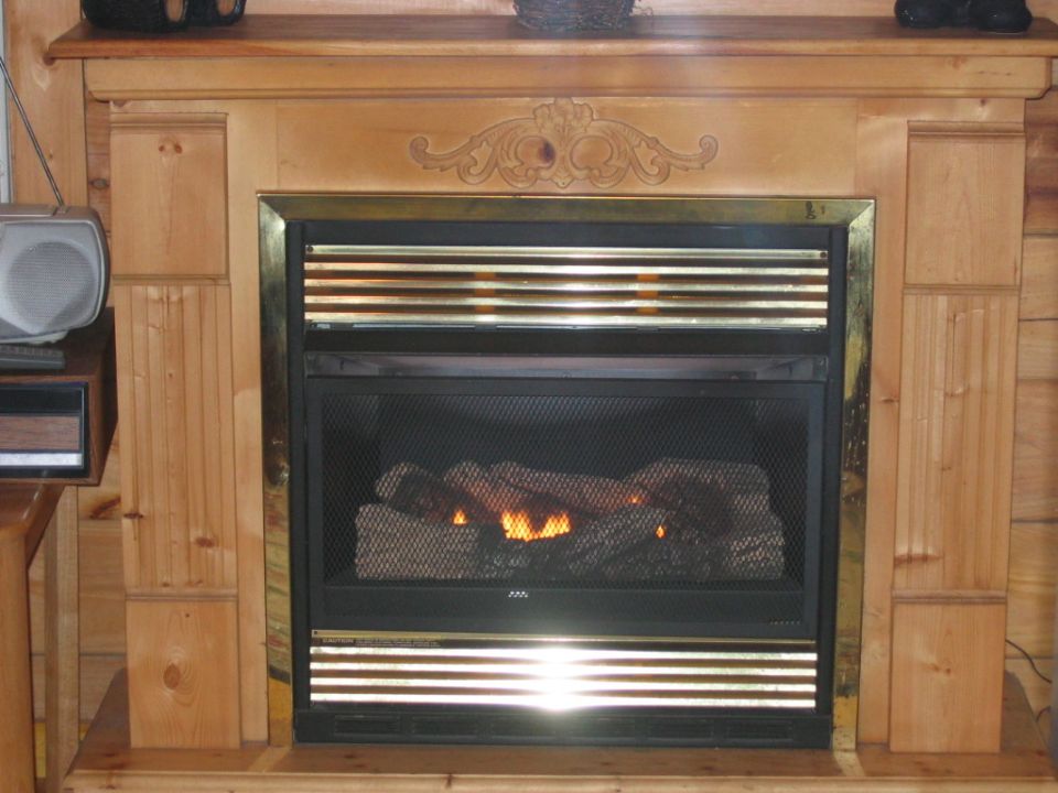 Gas fireplace with logs and flames, surrounded by a wooden mantel