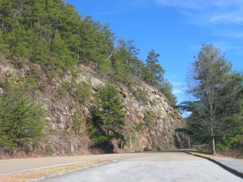 1985 Ford LTD Crown Victoria - A view of a road curving alongside a rocky cliff covered in pine trees on a clear day.