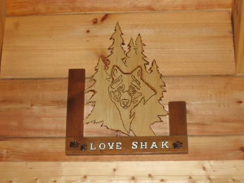 1985 Ford LTD Crown Victoria - A wooden carving of a wolf and trees is mounted on a wood-paneled wall, with the words 'LOVE SHAK' visible.