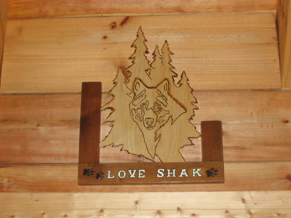 Wooden carving of a wolf in front of trees, with 'LOVE SHAK' text below